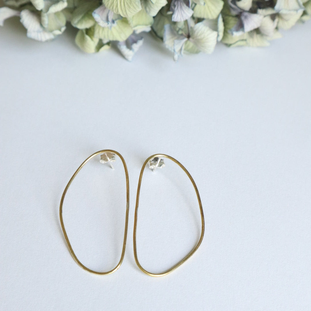 Gold hoop earrings on a light gray background with dried flowers.